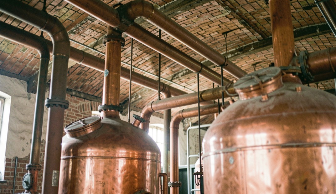 In einer alten Zuckerfabrik stehen hohe kupferne Kessel und dicke Rohrleitungen unter einem Gewölbedach aus Ziegeln.